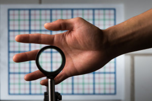 A multidirectional `perfect paraxial' cloak using 4 lenses. For a continuous range of viewing angles, the hand remains cloaked, and the grids seen through the device match the background on the wall (about 2 m away), in color, spacing, shifts, and magnification. The edges of the optics can be seen since this is a small-angle ('paraxial') cloak, but this can be reduced by using large optics and for distant viewing; also the center of the device must not be blocked. // an optical cloaking configuration designed by University of Rochester professor of physics John C. Howell and Ph.D. student Joseph Choi is pictured in Bausch & Lomb Hall September 11, 2014. // photo by J. Adam Fenster / University of Rochester